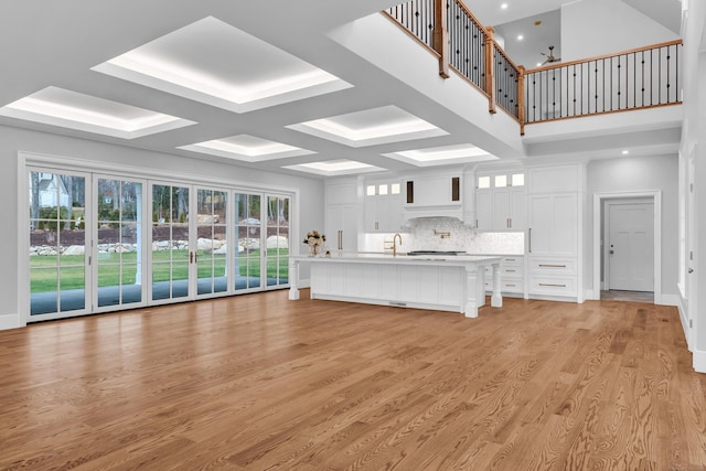 unfurnished living room featuring beam ceiling, light wood-type flooring, coffered ceiling, and sink