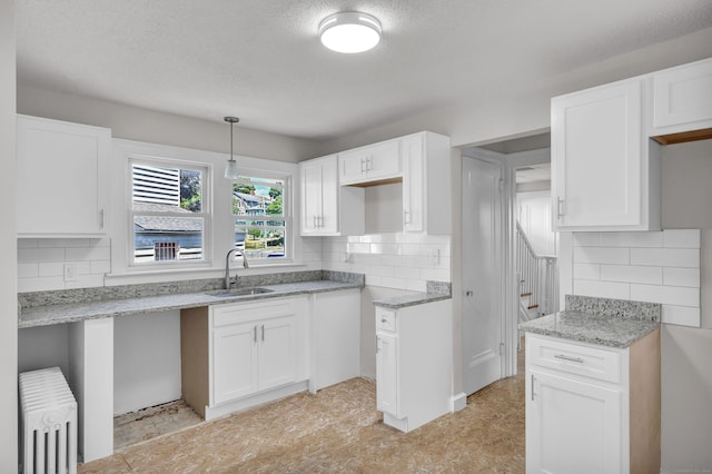 kitchen with backsplash, white cabinetry, radiator, and sink