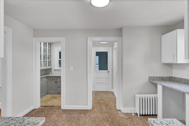 interior space featuring radiator, white cabinetry, light stone counters, a textured ceiling, and decorative backsplash