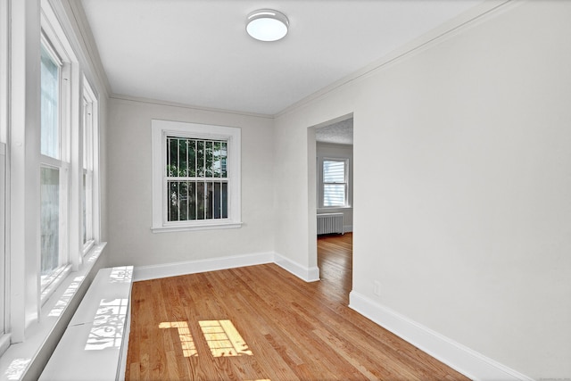 empty room featuring light hardwood / wood-style flooring, ornamental molding, and radiator heating unit