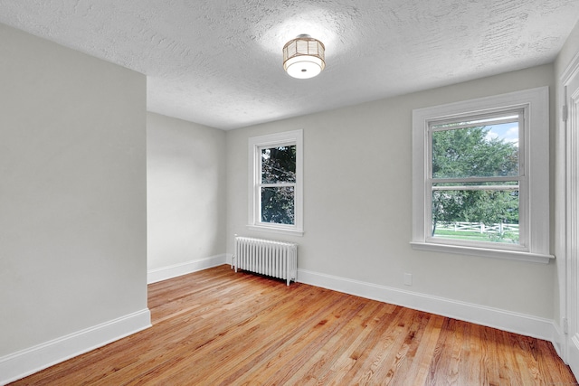 spare room featuring radiator heating unit, a textured ceiling, and light hardwood / wood-style flooring