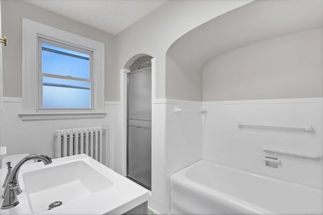 bathroom with a bathtub, sink, a textured ceiling, tile walls, and radiator heating unit