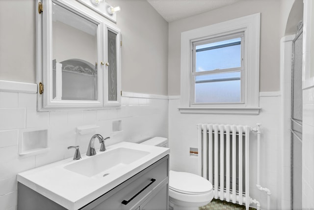 bathroom with radiator heating unit, vanity, tile walls, and toilet