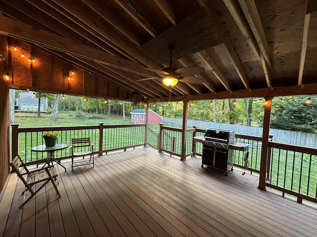 wooden terrace featuring a lawn, ceiling fan, a storage shed, and grilling area