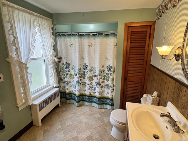 full bathroom with wood walls, shower / bath combination with curtain, sink, toilet, and radiator heating unit