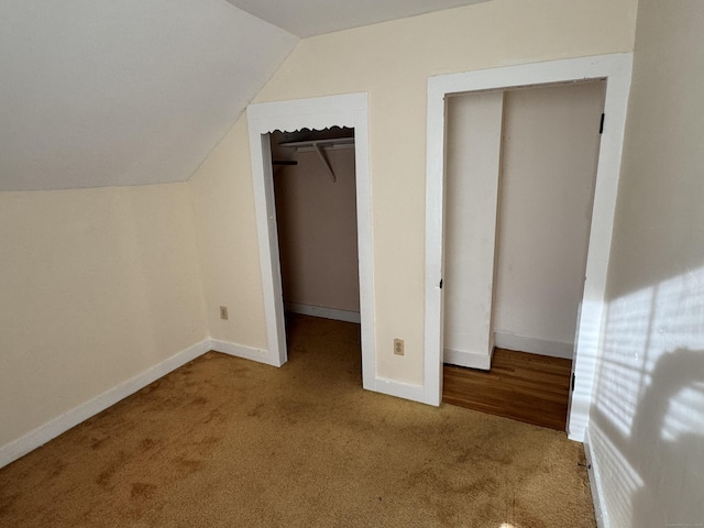 unfurnished bedroom with light carpet, a spacious closet, vaulted ceiling, and a closet