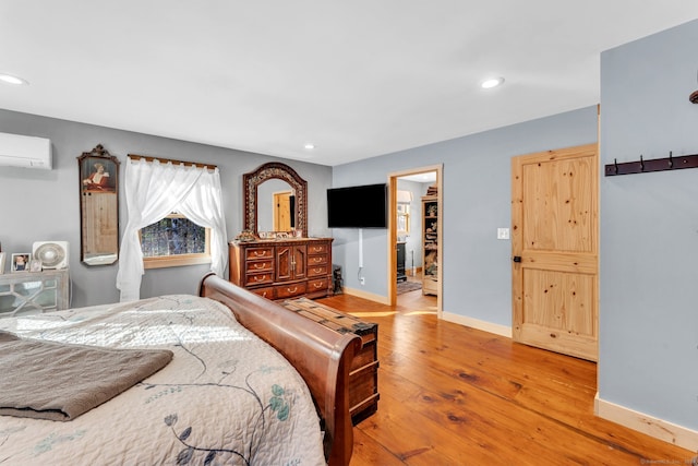 bedroom with light hardwood / wood-style floors, a walk in closet, and an AC wall unit