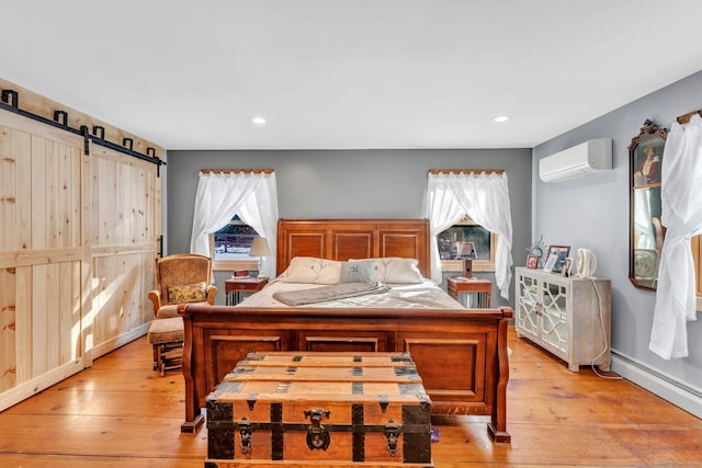 bedroom with a wall mounted AC, light hardwood / wood-style floors, a baseboard heating unit, and a barn door