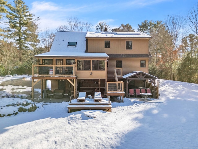 snow covered back of property with a sunroom and a wooden deck