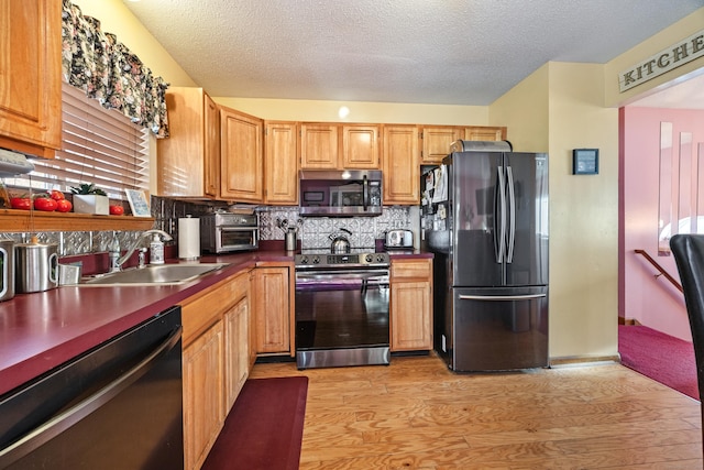 kitchen with dark countertops, decorative backsplash, light wood-style floors, stainless steel appliances, and a sink