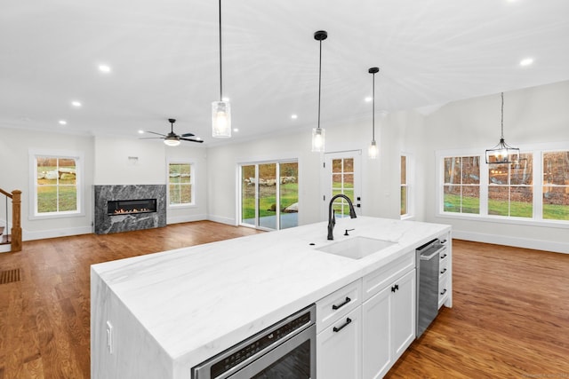 kitchen with a fireplace, sink, decorative light fixtures, a center island with sink, and white cabinets