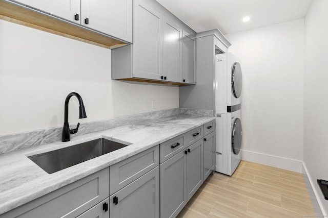 clothes washing area with cabinets, stacked washer / drying machine, and sink