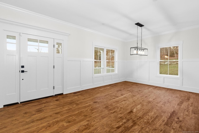 unfurnished dining area with ornamental molding, wainscoting, wood finished floors, and a decorative wall