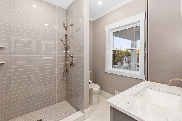 bathroom featuring toilet, ornamental molding, a tile shower, and vanity