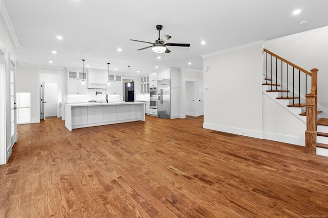 unfurnished living room with ceiling fan, stairway, wood finished floors, and ornamental molding