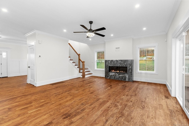 unfurnished living room with a high end fireplace, light wood-type flooring, ceiling fan, and crown molding