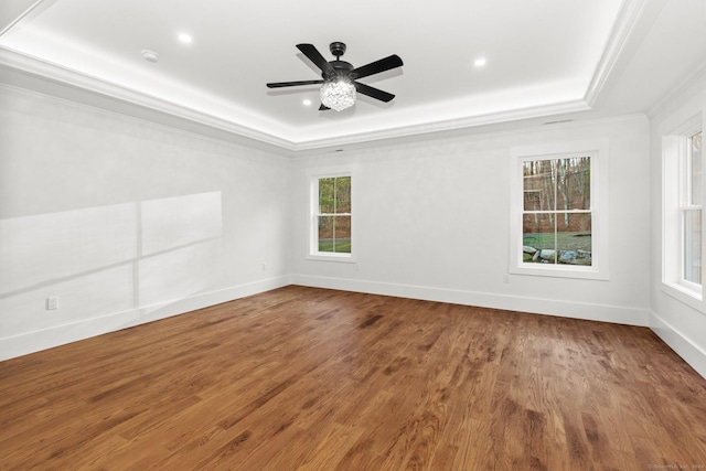 empty room with a tray ceiling, crown molding, baseboards, and wood finished floors