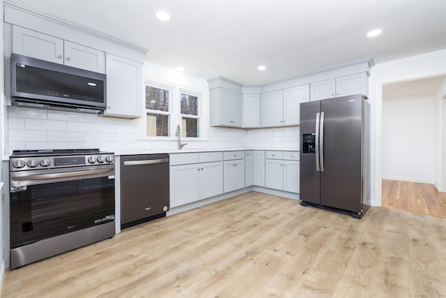 kitchen featuring sink, tasteful backsplash, light hardwood / wood-style floors, white cabinetry, and stainless steel appliances