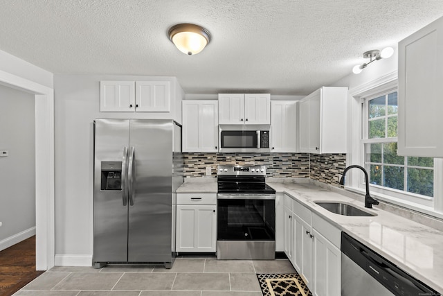 kitchen with white cabinets, stainless steel appliances, light stone countertops, and sink