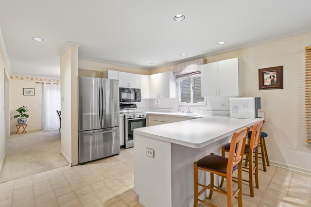 kitchen with kitchen peninsula, appliances with stainless steel finishes, a breakfast bar, sink, and white cabinetry