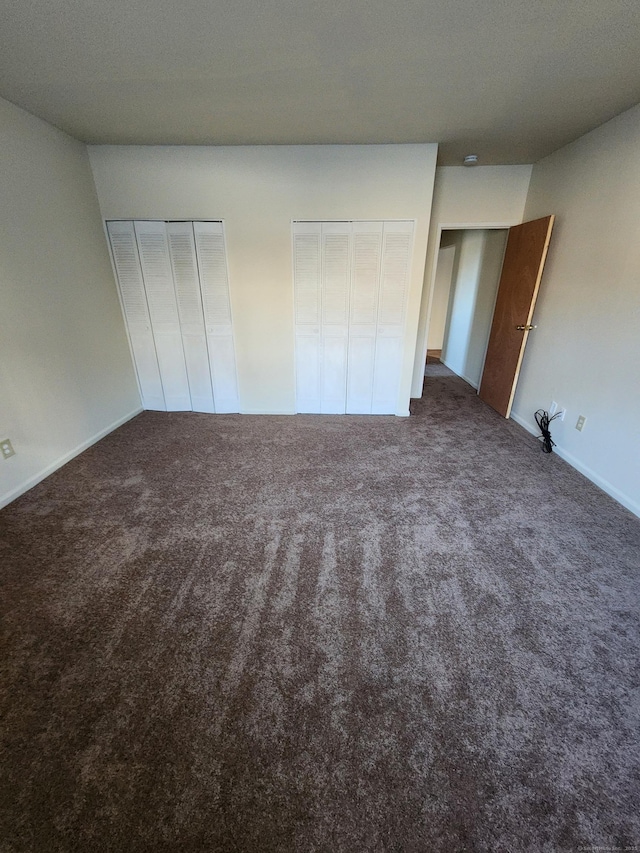 unfurnished bedroom featuring multiple closets and dark carpet