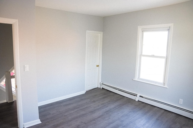 spare room featuring dark wood-type flooring, a baseboard radiator, and a healthy amount of sunlight