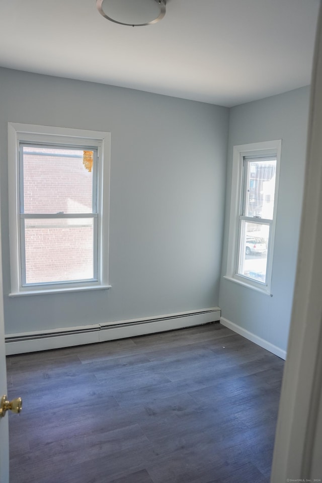 empty room with dark hardwood / wood-style floors, baseboard heating, and plenty of natural light