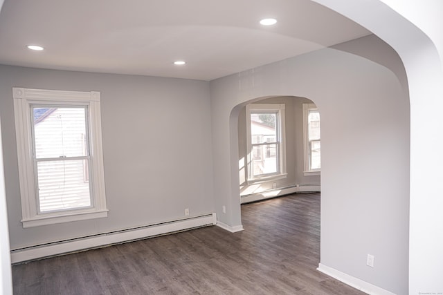 unfurnished room with dark hardwood / wood-style floors, a healthy amount of sunlight, and a baseboard heating unit