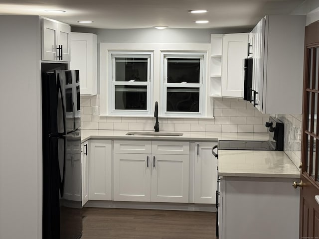 kitchen with sink, white cabinetry, black fridge, and tasteful backsplash