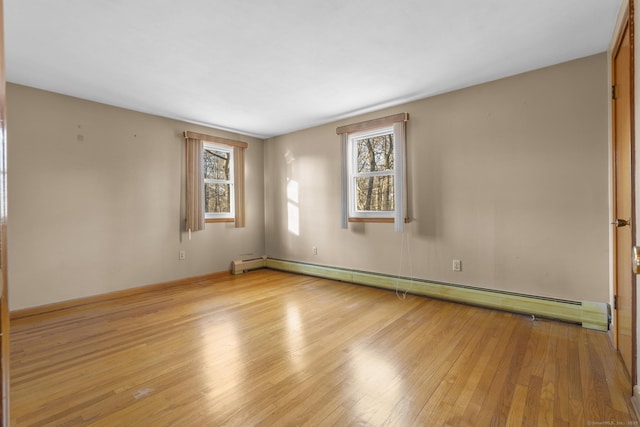 empty room with a baseboard heating unit, baseboards, plenty of natural light, and light wood finished floors