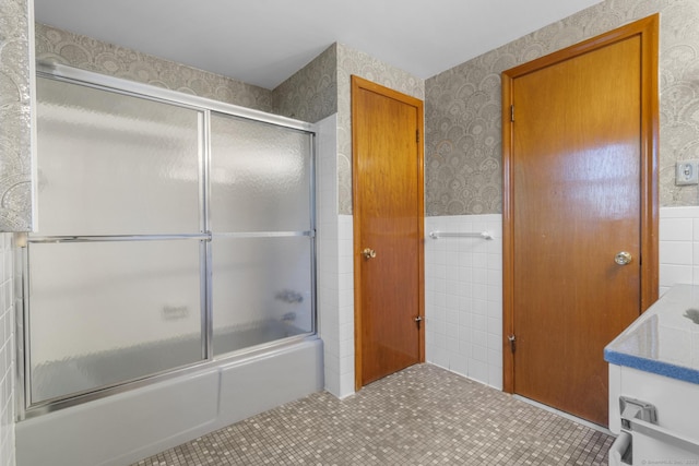 full bathroom with wallpapered walls, wainscoting, shower / bath combination with glass door, tile patterned floors, and tile walls