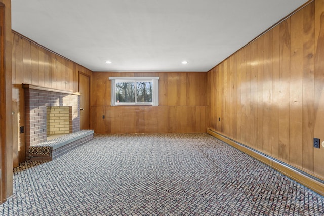 carpeted empty room with a brick fireplace, wooden walls, and baseboard heating