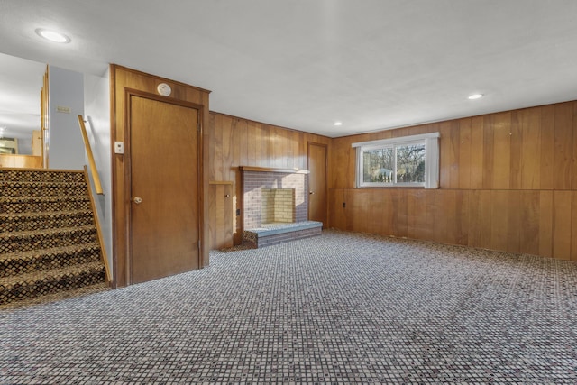 unfurnished living room featuring carpet, wood walls, and a brick fireplace