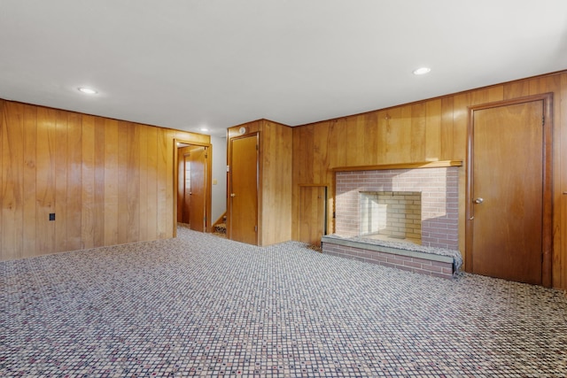 unfurnished living room featuring carpet floors, wood walls, a brick fireplace, and recessed lighting