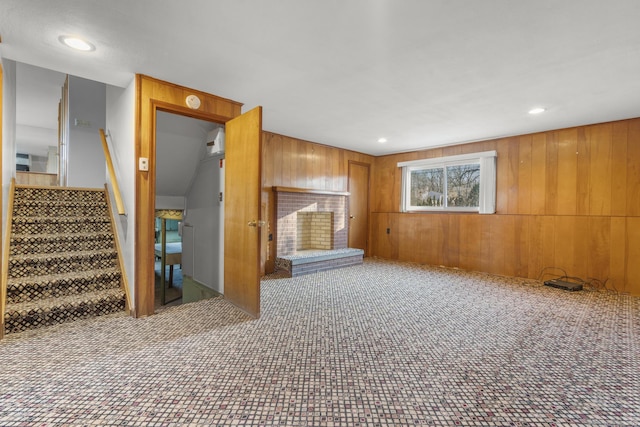 unfurnished living room featuring recessed lighting, carpet flooring, wooden walls, and stairs