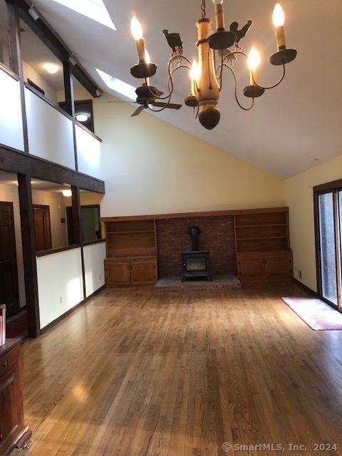 unfurnished living room featuring beam ceiling, a wood stove, a skylight, an inviting chandelier, and hardwood / wood-style floors