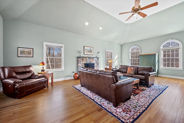 living room featuring a stone fireplace, ceiling fan, hardwood / wood-style floors, and lofted ceiling