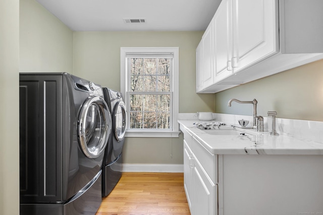 clothes washing area featuring cabinets, independent washer and dryer, sink, and light hardwood / wood-style flooring