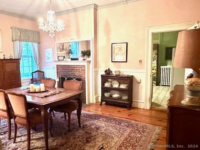 dining space with ornamental molding, hardwood / wood-style flooring, a notable chandelier, a fireplace, and radiator heating unit