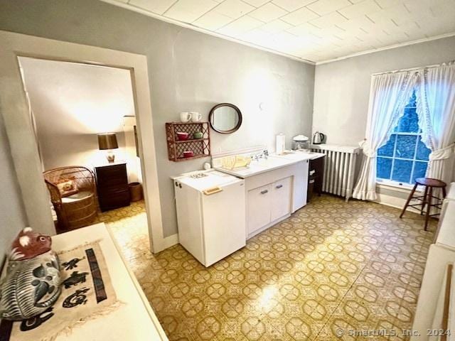 kitchen with radiator, white cabinetry, sink, white refrigerator, and ornamental molding