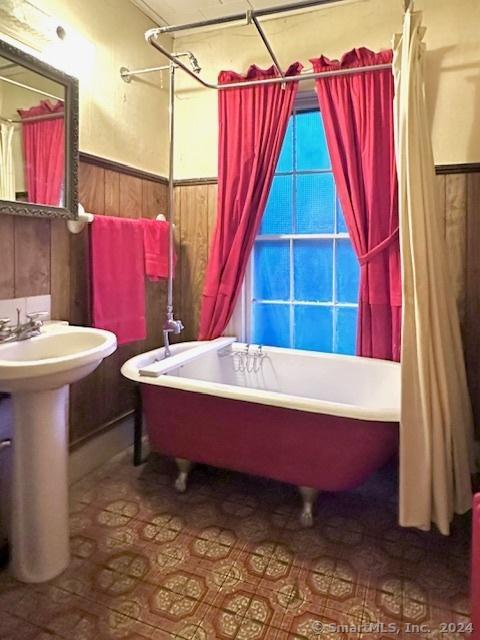 full bath with a shower with curtain, a wainscoted wall, wood walls, and a tub