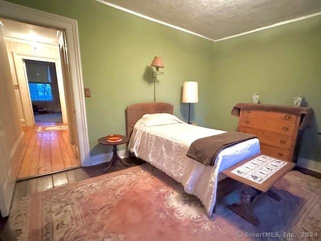 bedroom featuring baseboards, crown molding, wood finished floors, and a textured ceiling