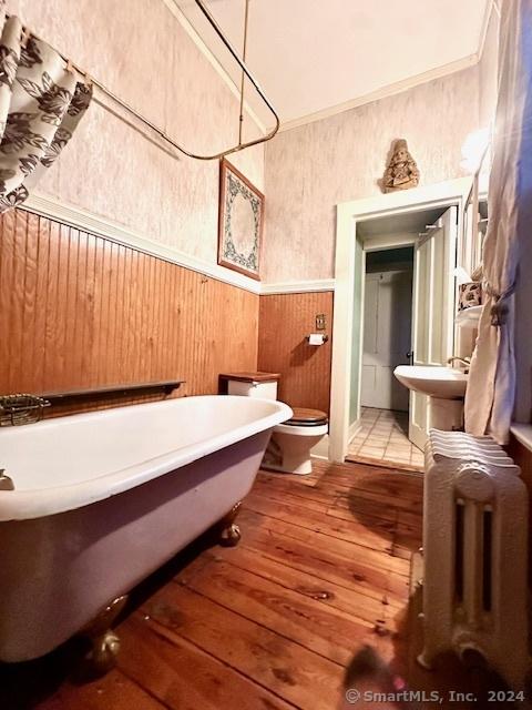 bathroom with hardwood / wood-style floors, a bathtub, wood walls, toilet, and radiator heating unit