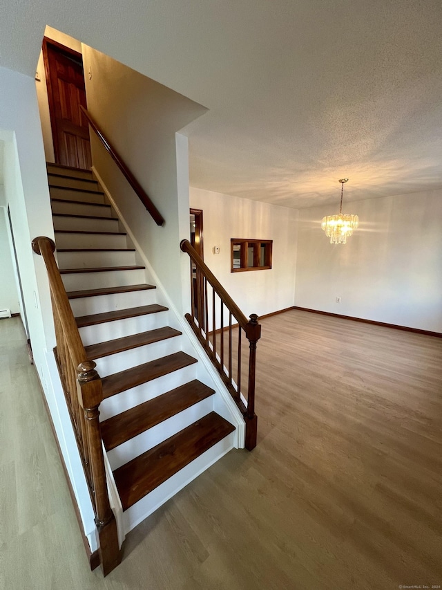 stairs with wood-type flooring, a textured ceiling, and an inviting chandelier