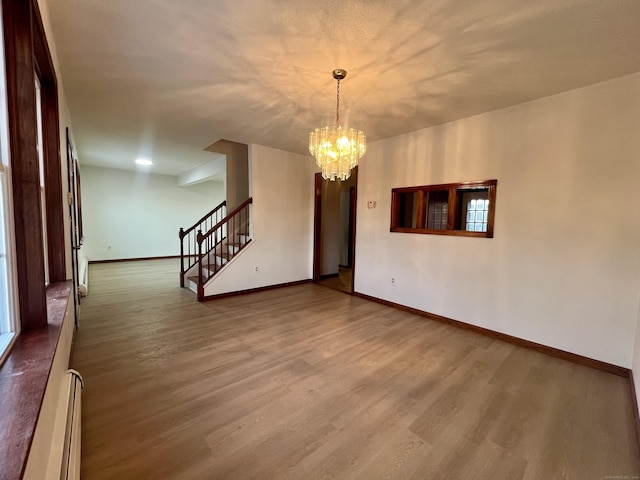 empty room featuring hardwood / wood-style floors, a baseboard heating unit, and a chandelier