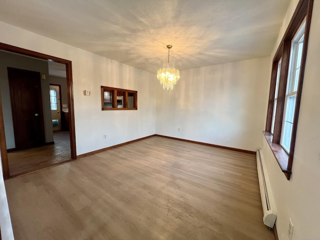 spare room with wood-type flooring, a baseboard radiator, a notable chandelier, and a healthy amount of sunlight