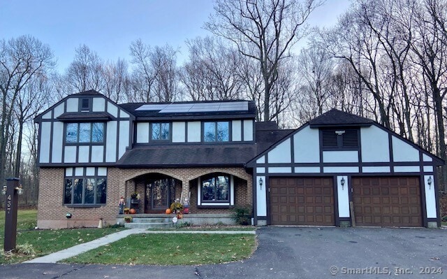 english style home with solar panels, a porch, and a garage