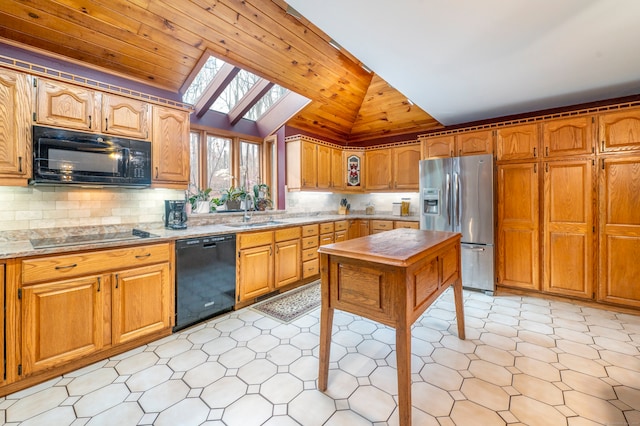 kitchen featuring backsplash, light stone counters, lofted ceiling with skylight, sink, and black appliances