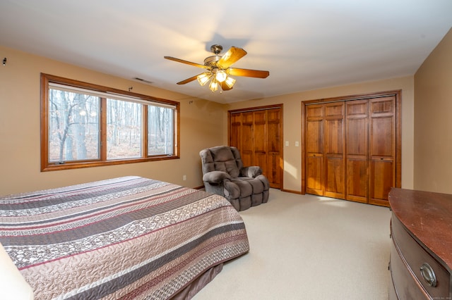 carpeted bedroom with ceiling fan and two closets