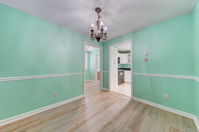 spare room with light wood-type flooring, an inviting chandelier, and a textured ceiling